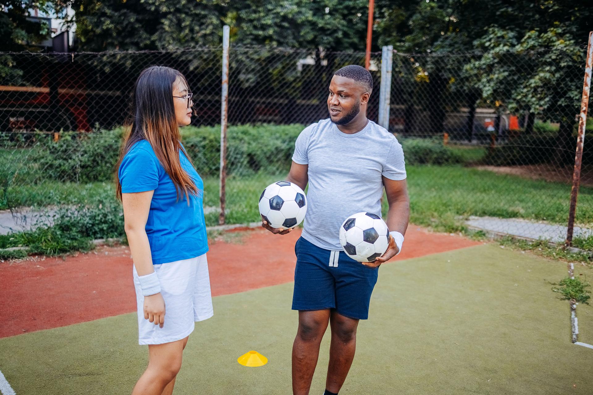 Two young adults practicing football on sport field in city block