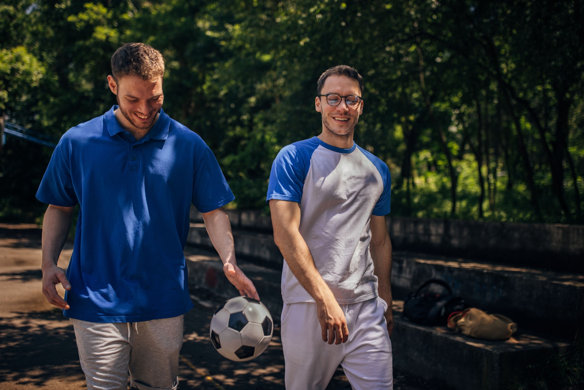 Two men walking one holding a soccer ball in hand.