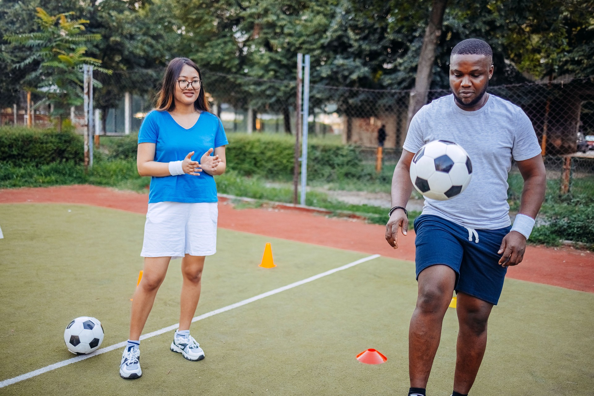 Two young adults practicing football on sport field in city block