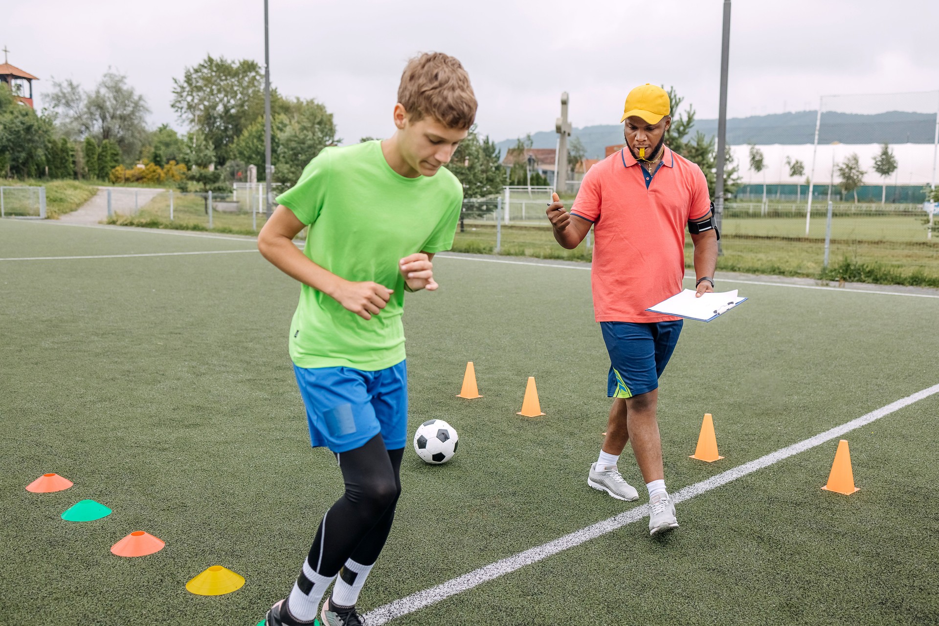 Boy having individual soccer training by the black coach on sport field