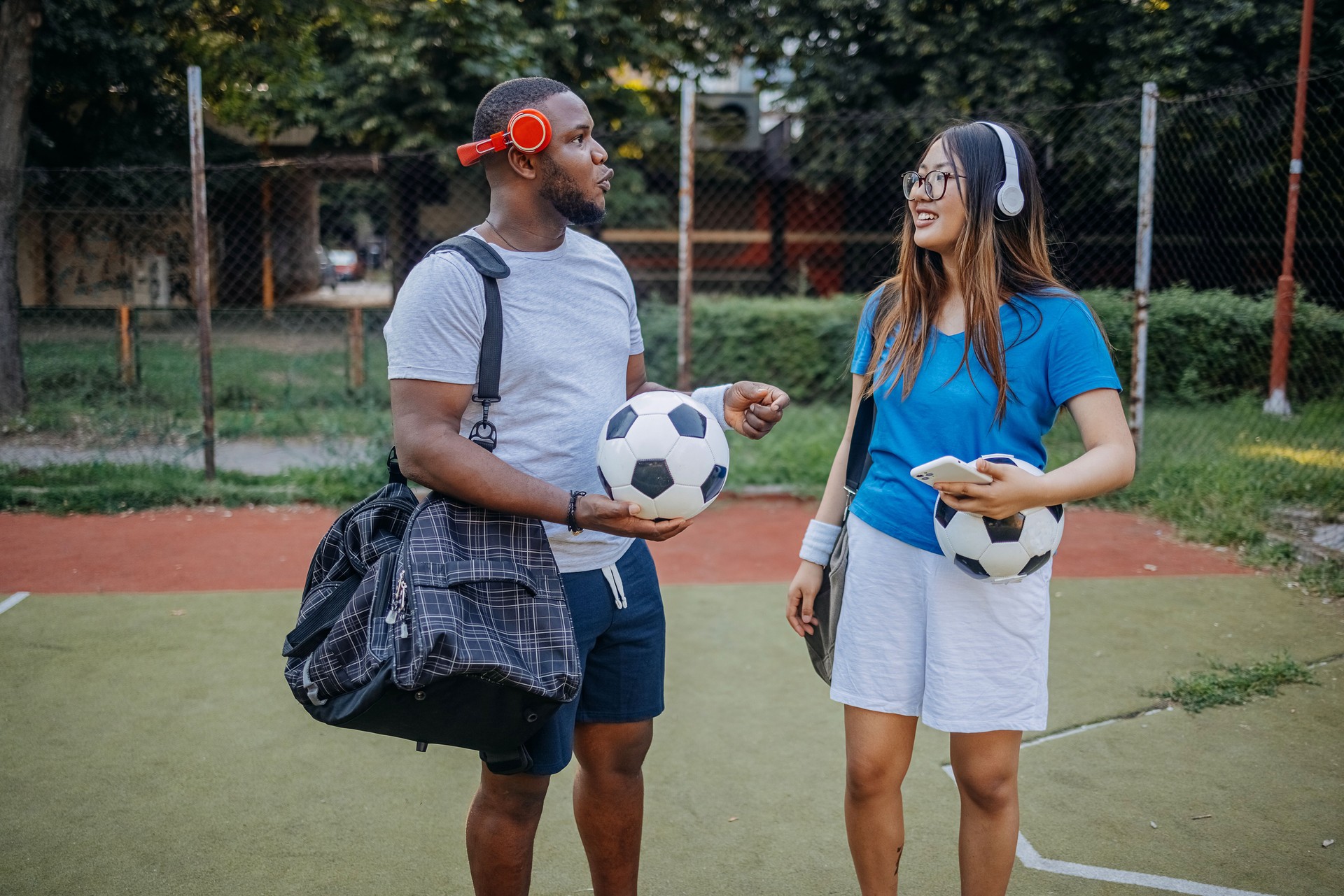 Two young adults going on football training on sport field in city block